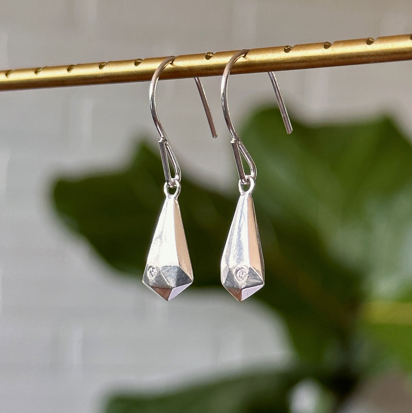 Silver and Diamond Crystal Fragment Earrings hanging in front of a white brick wall, side angle