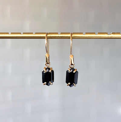 Eloise Black Garnet Earrings in Vermeil hanging in front of a white brick wall, front angle