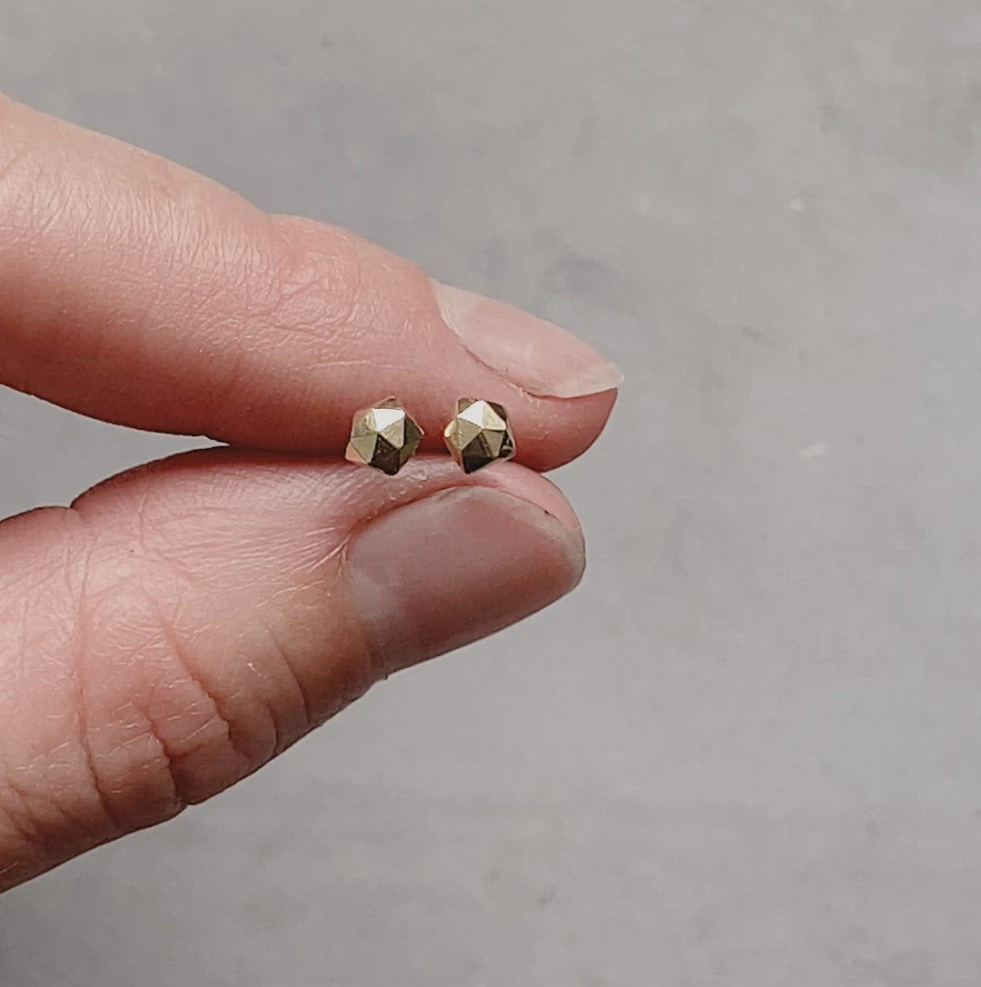 14k yellow gold geometric faceted stud earrings in the micro size between two fingers by Corey Egan