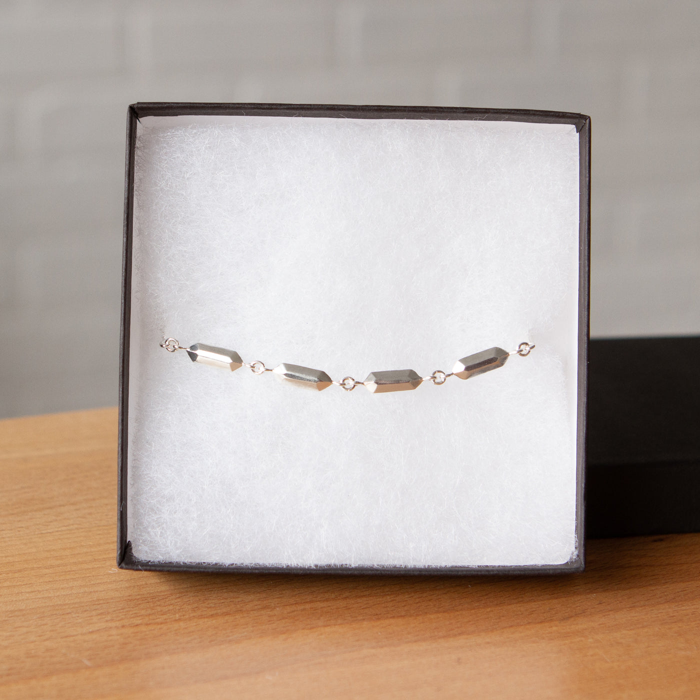 Fragment Link Bracelet in Silver on a wooden table in packaging 