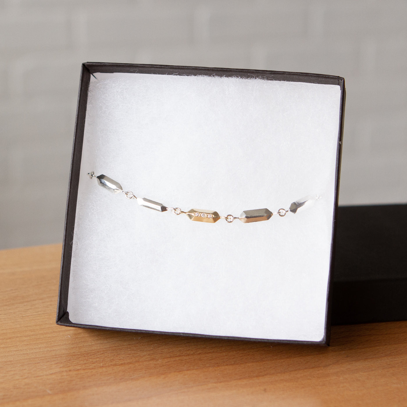 Fragment Link Bracelet with Gold Link on wooden table in packaging