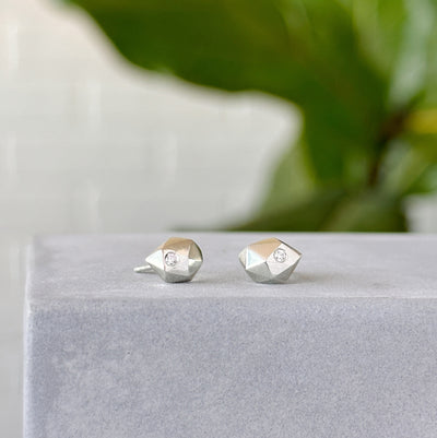 Tiny Fragment Diamond Stud Earrings sitting on concrete in front of a white wall, side angle