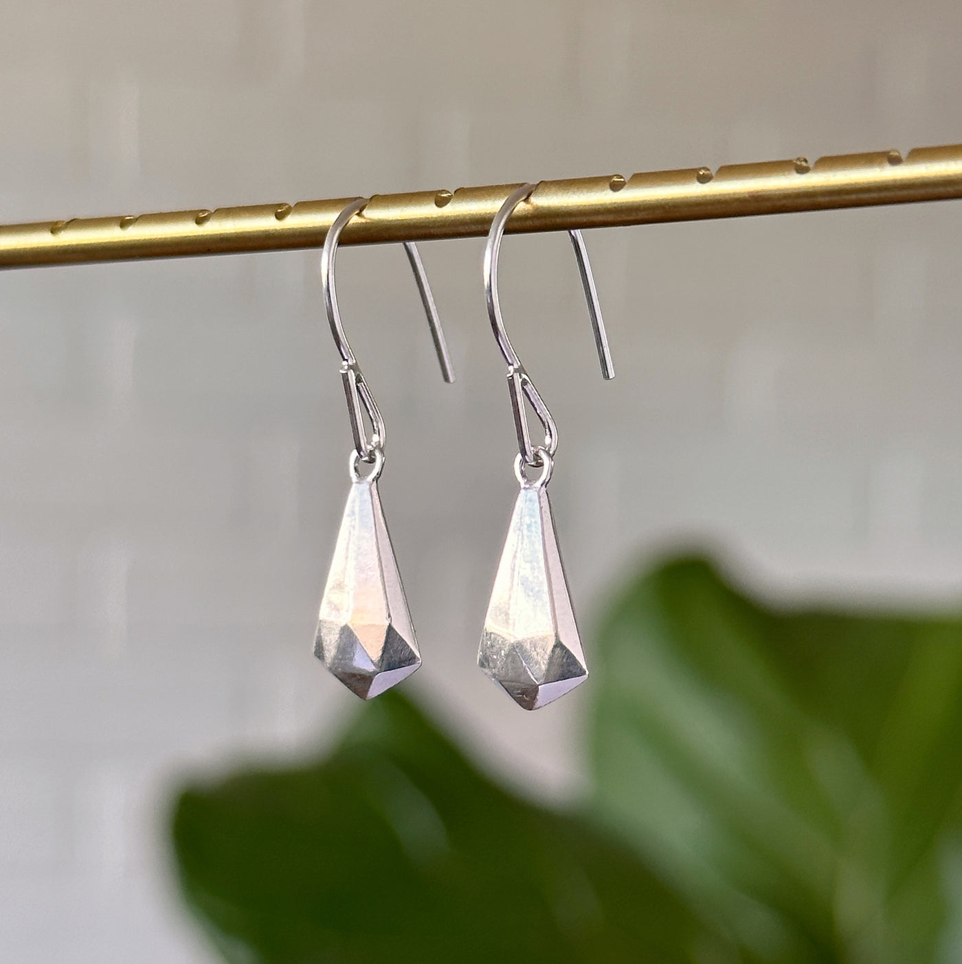 Silver Crystal Fragment Earrings hanging in front of a white wall, side angle