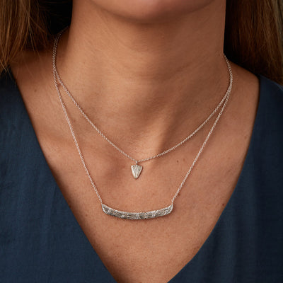 Sterling silver curved bar necklace with five scattered diamonds and an engraved sunburst pattern radiating from each on a neck | Corey Egan 