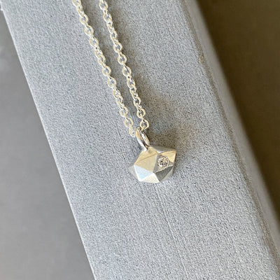 Sterling silver wabi-sabi faceted geometric necklace with a single diamond facet by Corey Egan on concrete