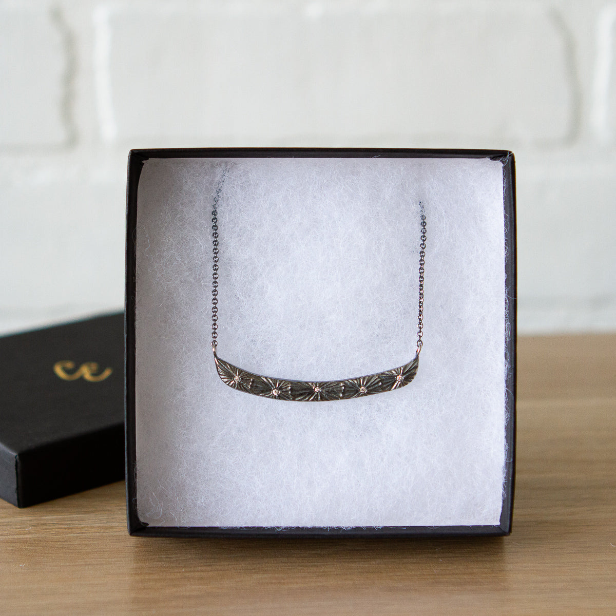 Oxidized silver bar necklace with a sunburst motif and five scattered diamonds in a gift box
