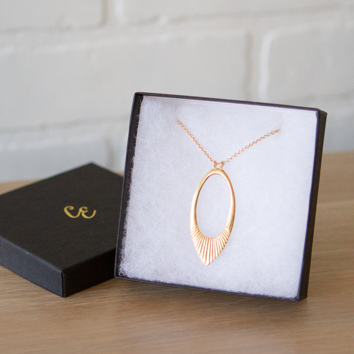 Ectra long neckalce with large open petal shape pendant with carved ray texture across the bottom in a gift box