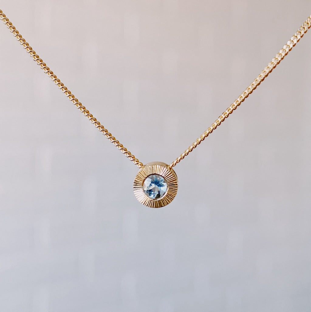 March birthstone 14k yellow gold Aurora necklace with aquamarine center and engraved sunburst halo border.