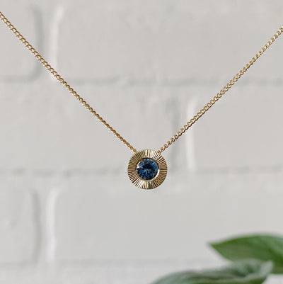 14k yellow gold Medium aurora necklace with a denim blue Montana sapphire center and engraved halo border in natural light
