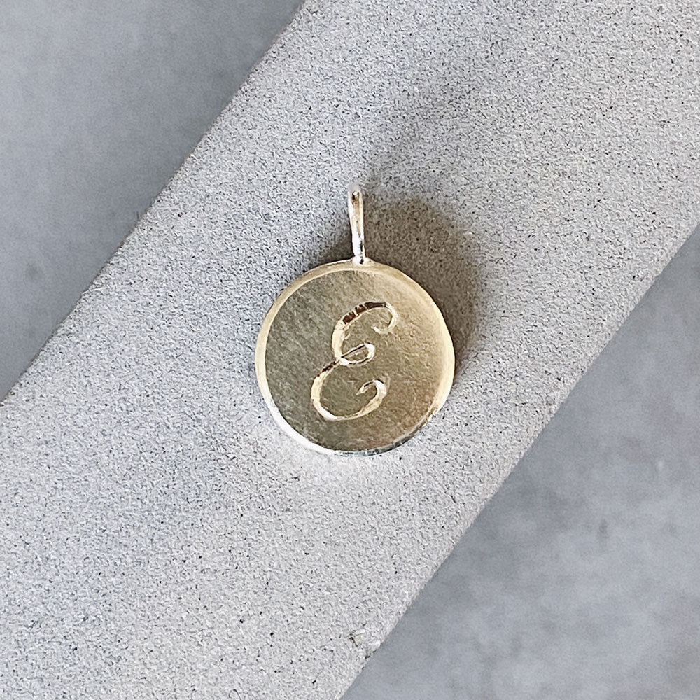 Round sterling silver pendant with a hand-engraved script "E" initial letter