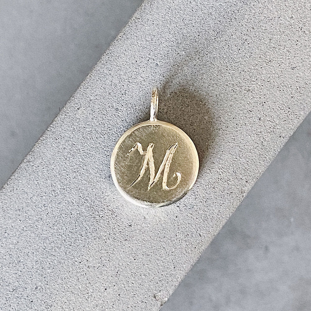Round sterling silver pendant with a hand-engraved script "M" initial letter