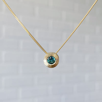 14k yellow gold medium Aurora necklace with a round teal green indicolite tourmaline center and engraved rays halo border in natural light