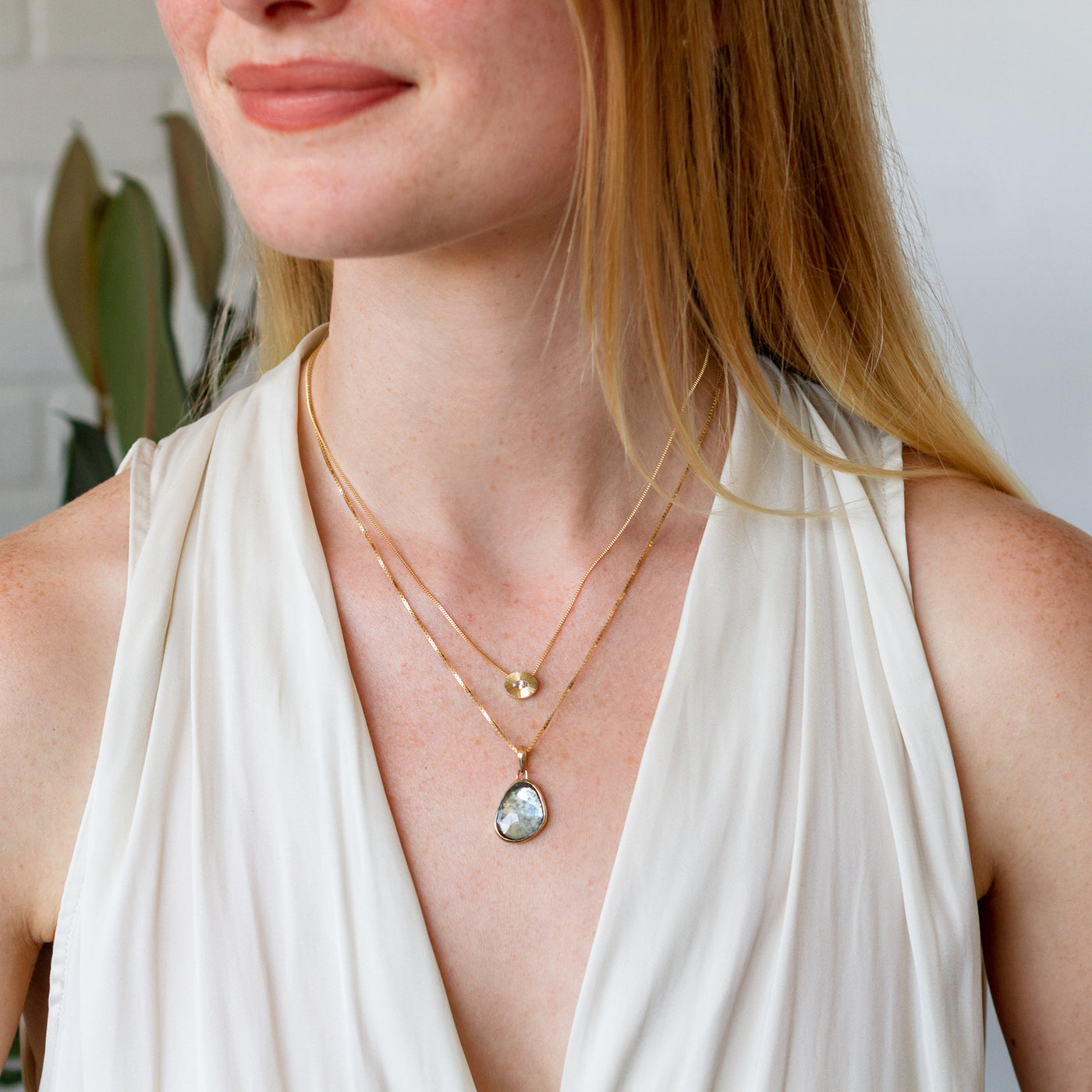 A model wears the moss aquamarine silver and gold bijou pendant on a gold box chain layered with the step nouveau diamond oval aurora necklace