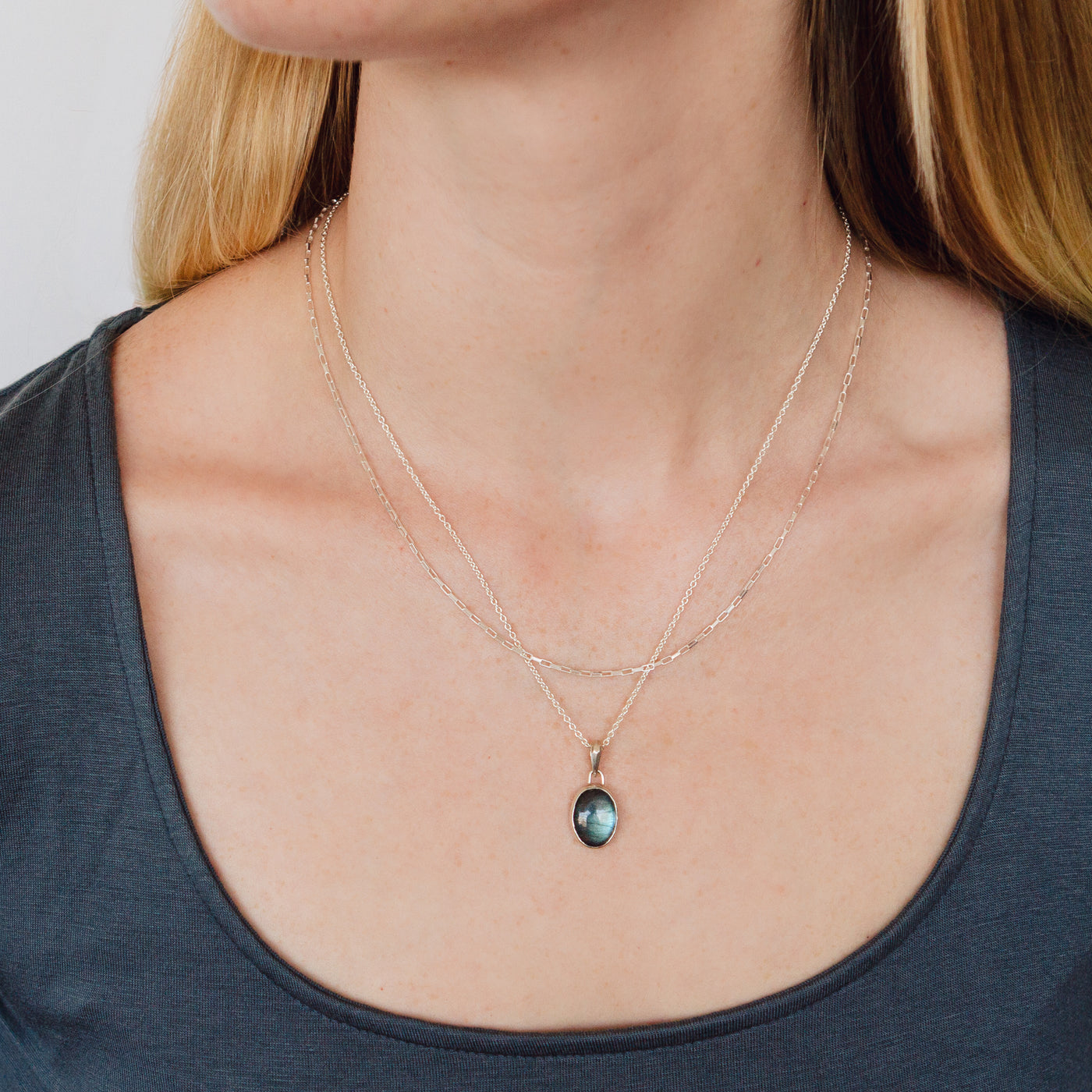 Smooth Oval Labradorite cabochon in a sterling silver bezel with a faceted bail around a neck layered with a link chain