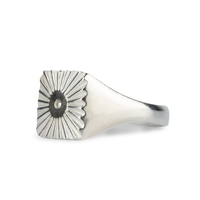 Side view Large silver square signet ring with a carved sunburst pattern and single silver bead in the center on a white background