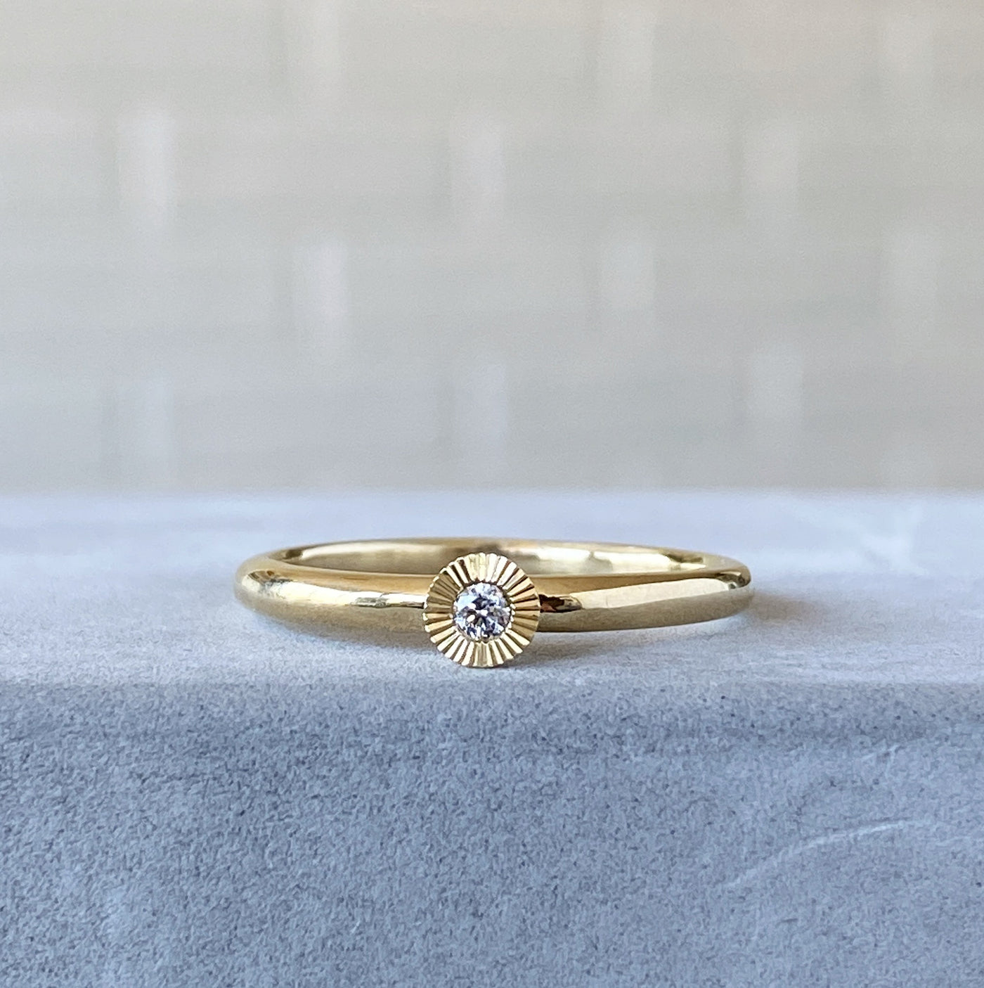 14k yellow gold small aurora stacking ring with a 2mm center diamond and engraved border on concrete