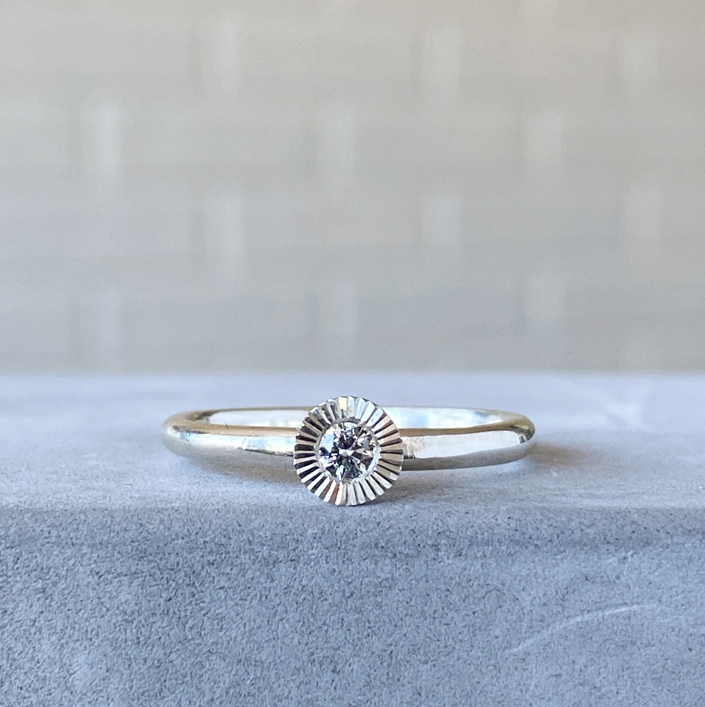 sterling silver large aurora stacking ring with a 3mm center diamond and engraved border resting on concrete