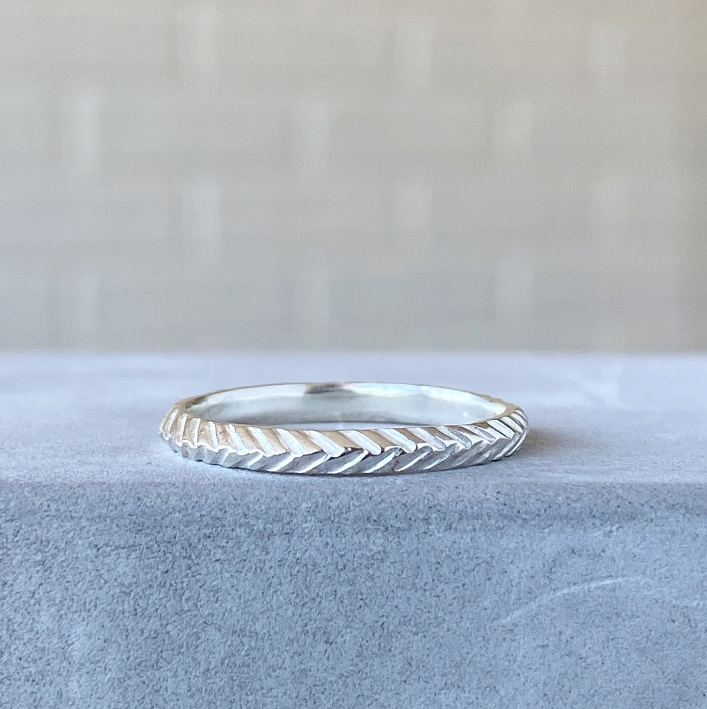 sterling silver stackable herringbone carved band 2mm width resting on concrete
