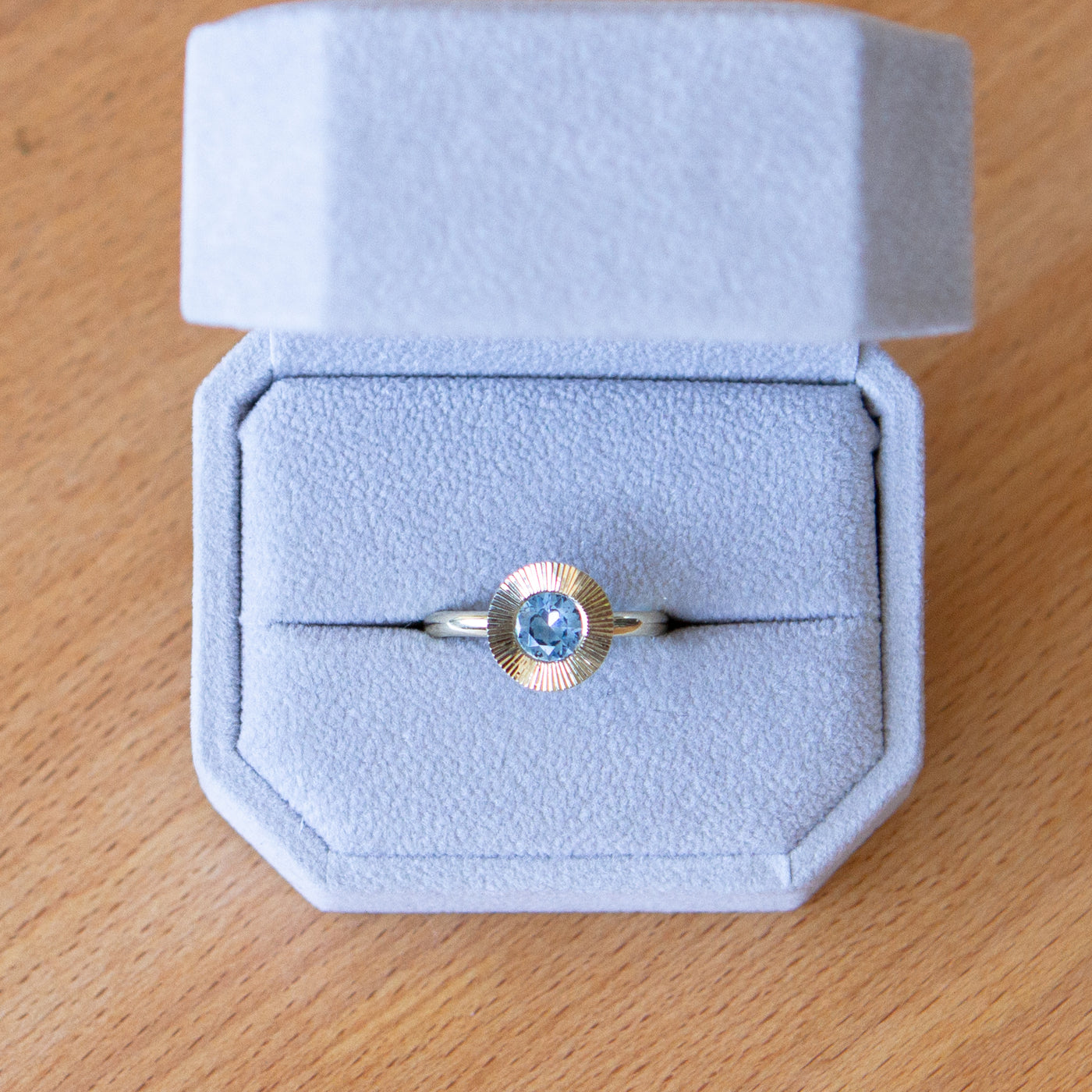 Round Medium Blue Montana sapphire in a 14k yellow gold Aurora ring with an engraved halo border in a ring box