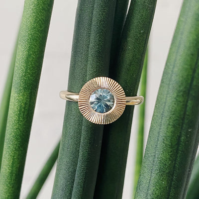 Round mint green Montana sapphire in a 14k yellow gold Aurora ring with an engraved halo border in natural light