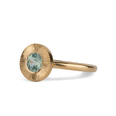 Side view of Round mint green Montana sapphire in a 14k yellow gold Aurora ring with an engraved halo border on a white background