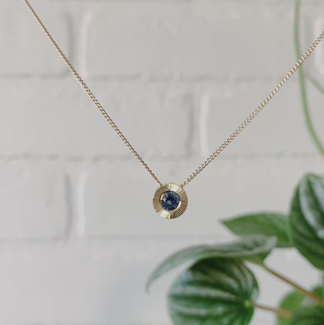14k yellow gold Medium aurora necklace with a denim blue Montana sapphire center and engraved halo border