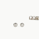 Pair of round silver ball stud earrings with white diamonds on a white background