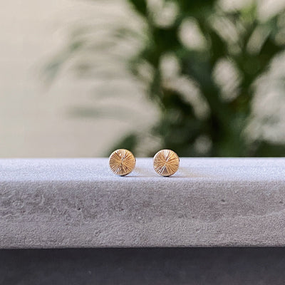 Tiny engraved gold stud earring by Corey Egan on concrete