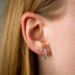silver rise stud earrings with engraving on an ear with a herringbone stud earring