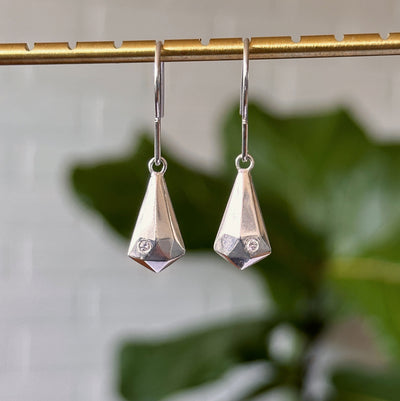 Silver and Diamond Crystal Fragment Earrings hanging in front of a white brick wall, front angle