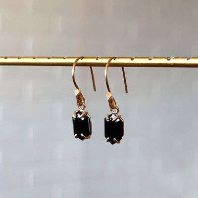 Eloise Black Garnet Earrings in Vermeil hanging in front of a white brick wall, side angle