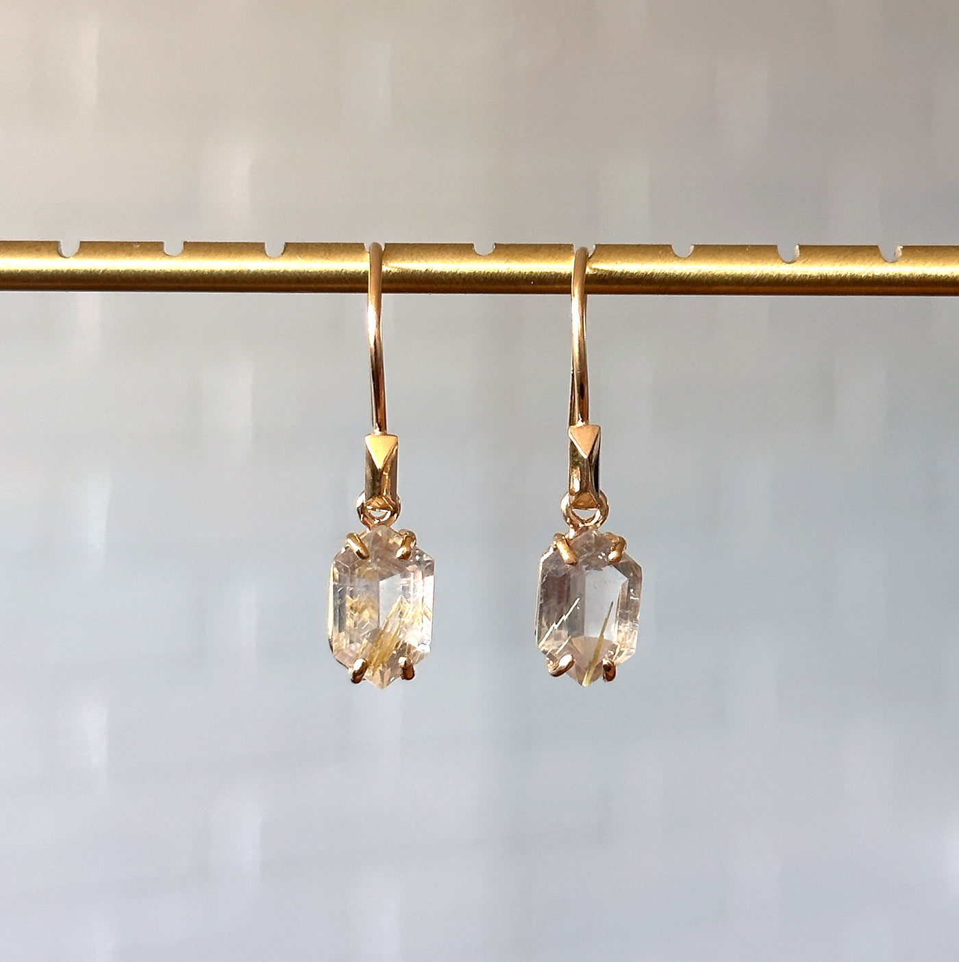 Eloise Rutilated Quartz Earrings in Vermeil hanging in front of a white brick wall, front angle
