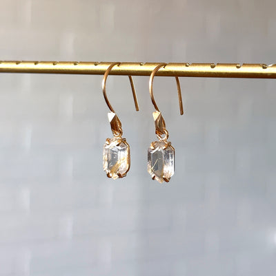 Eloise Rutilated Quartz Earrings in Vermeil hanging in front of a white brick wall, side angle