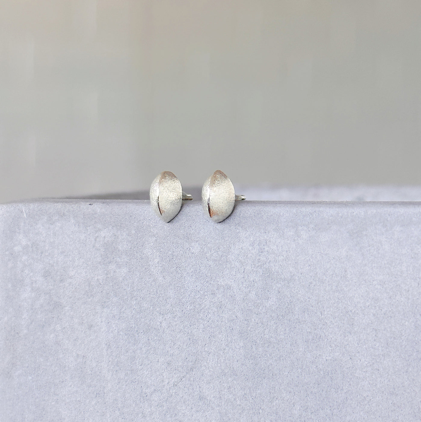 Silver Dewdrop Studs on a concrete table in front of a white wall, side angle