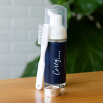 Foaming Jewelry Cleaner on a wooden table in front of a white wall, brush standing upright