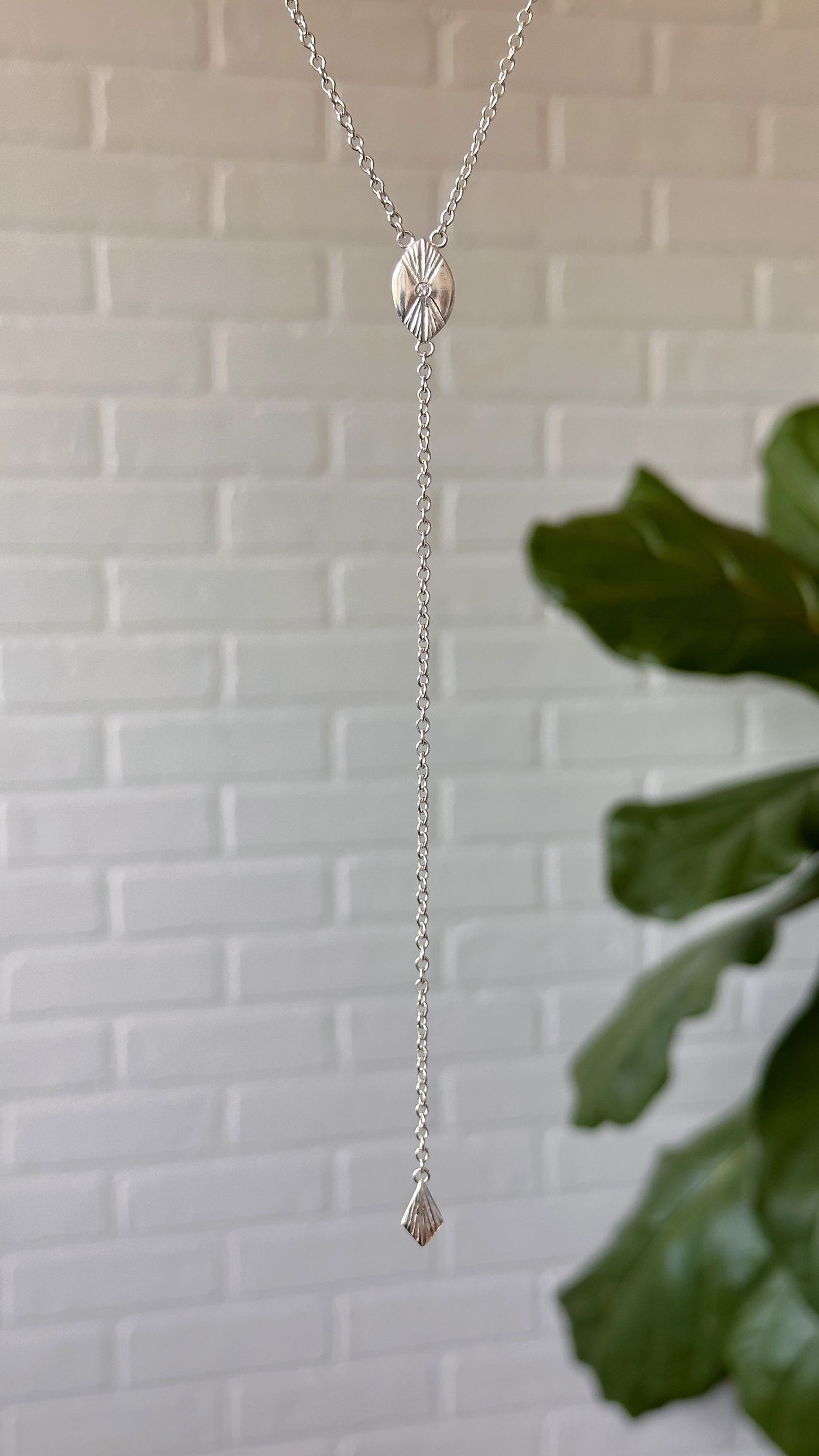 Prism Lariat in silver hanging in front of a white brick wall