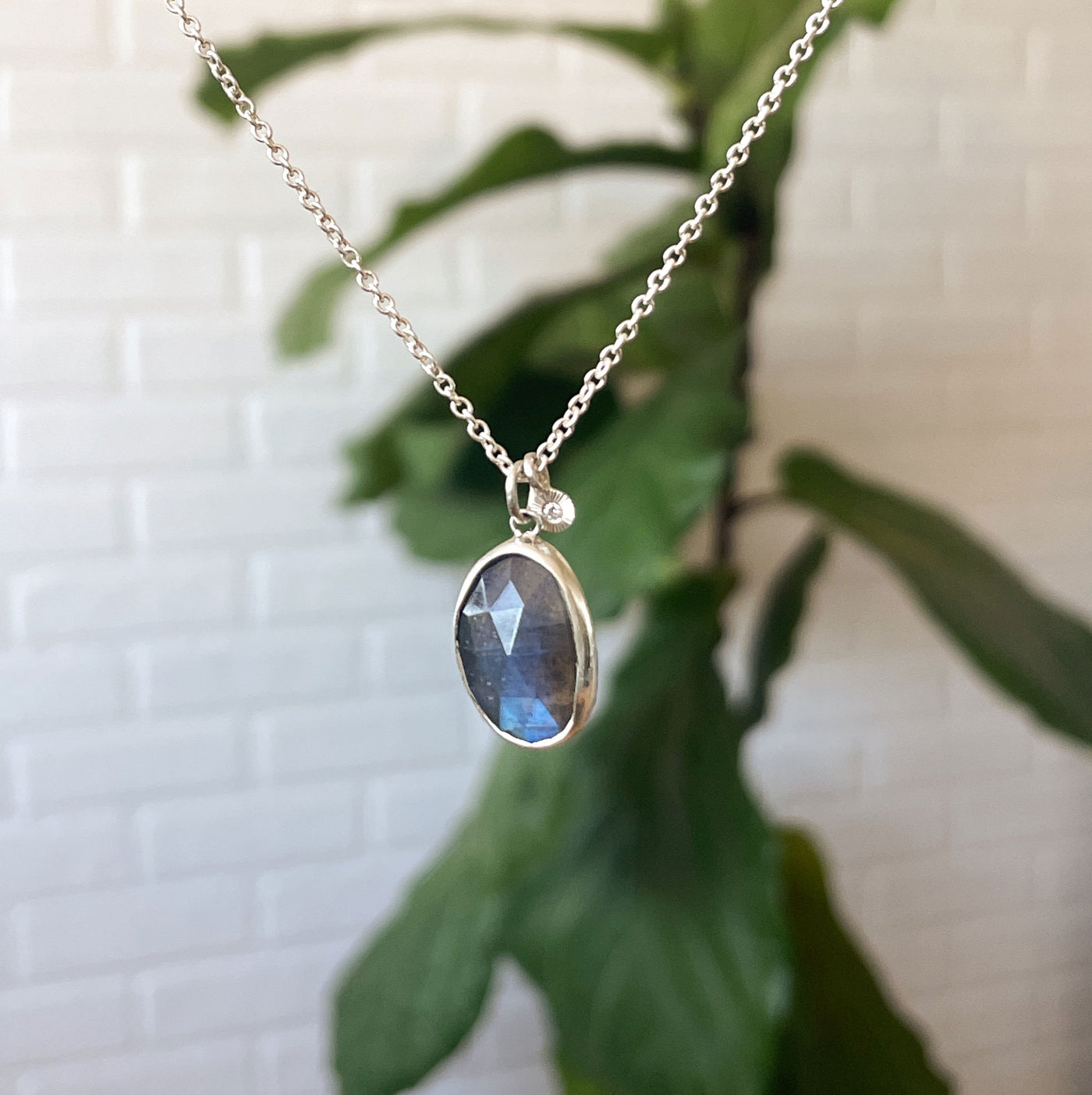 Rose Cut Labradorite Theia Necklace in Sterling Silver hanging in front of a white wall, side angle