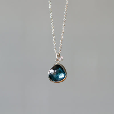Rose Cut London Blue Topaz Silver Theia Necklace #9 hanging in front of a white wall, front angle