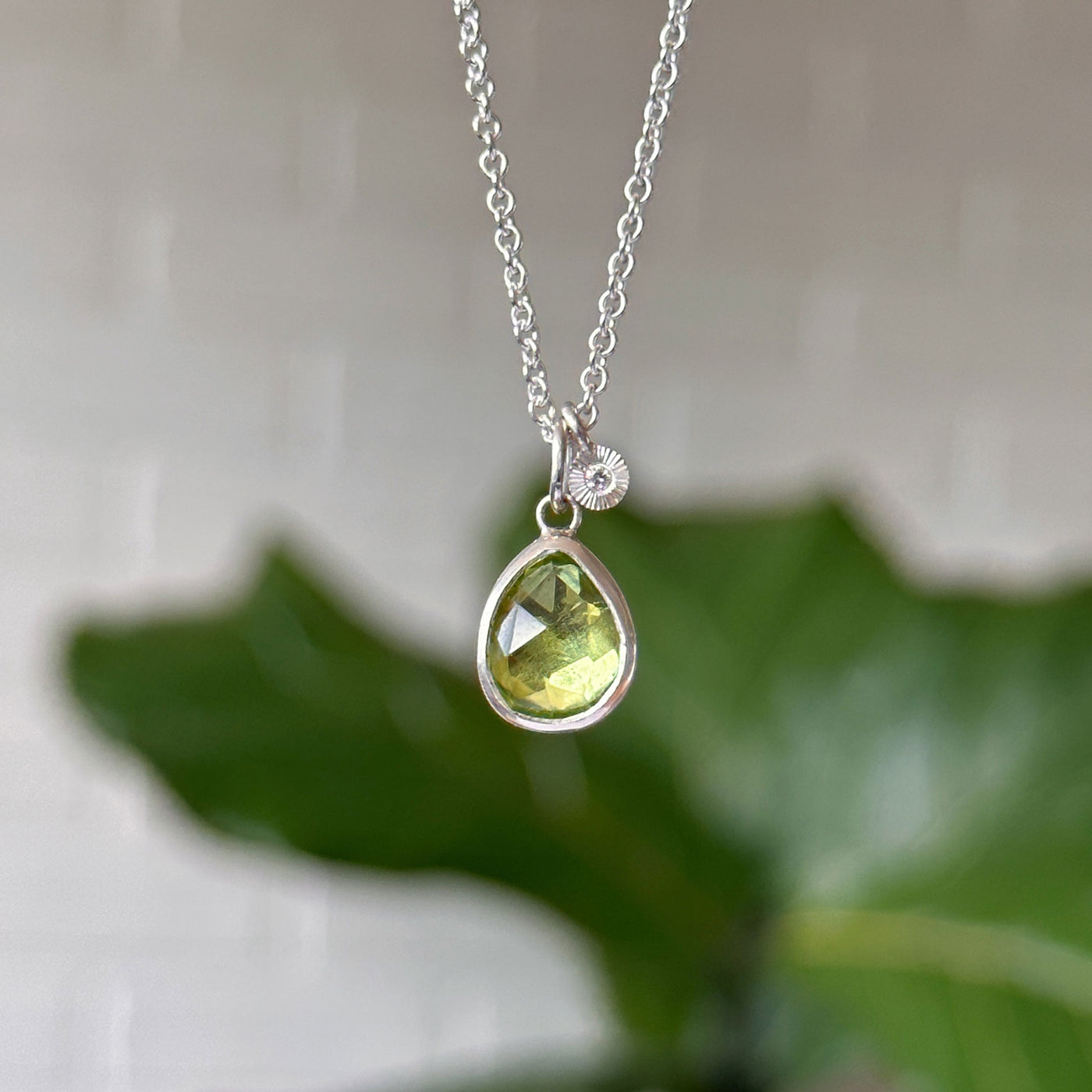 Peridot Theia Necklace in Sterling Silver #2 hanging in front of white wall, front angle
