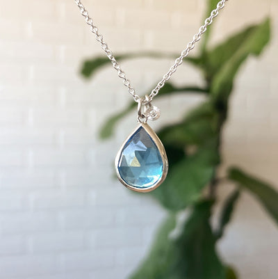 Swiss Blue Topaz Theia Necklace in Sterling Silver #1 hanging in front of a white wall, front angle