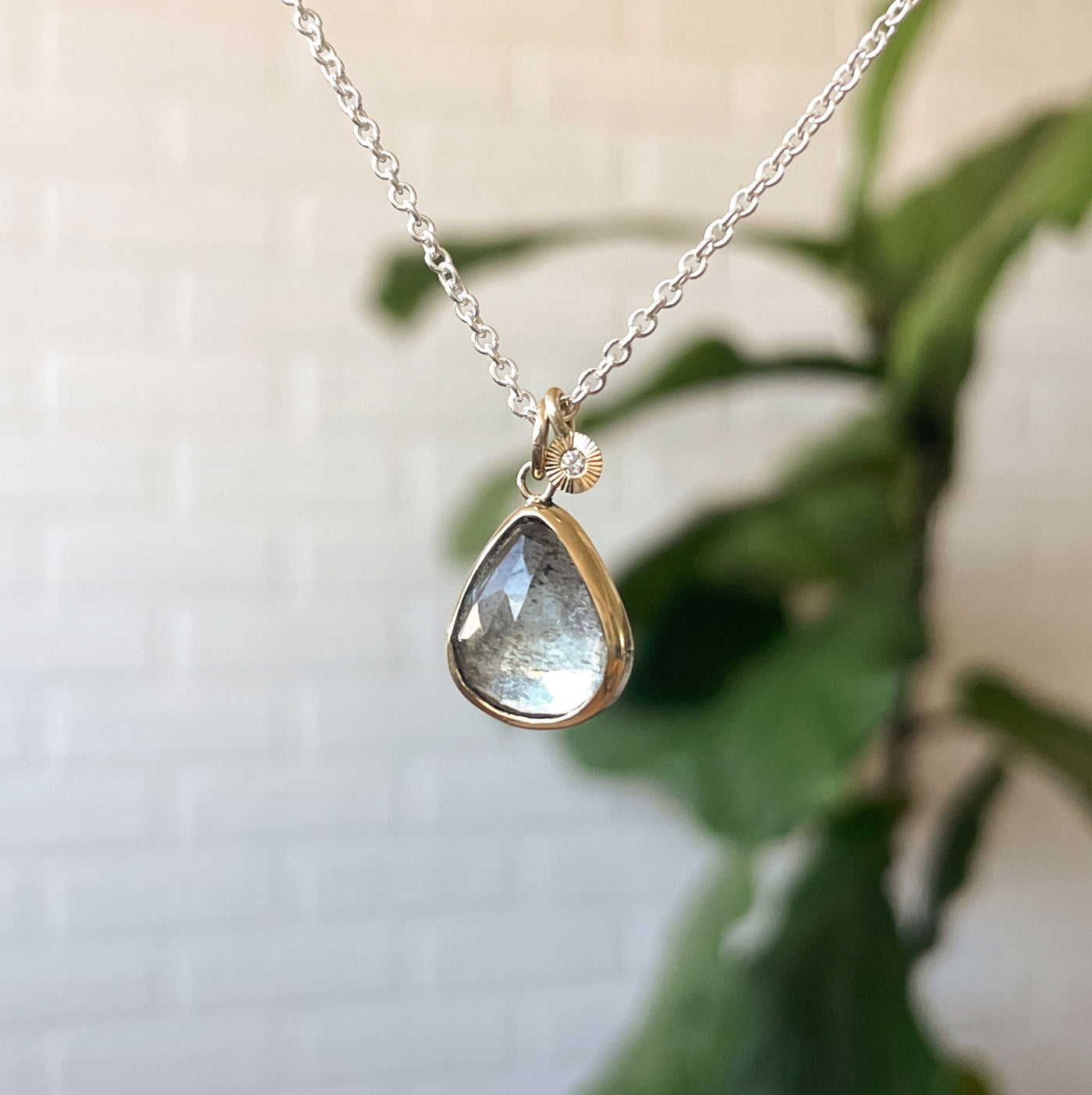 Moss Aquamarine Theia Necklace in Sterling Silver and Gold #4 hanging in front of a white wall, front angle