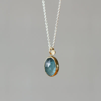 Rose Cut Moss Aquamarine Silver and Gold Theia Necklace #6 hanging in front of a wall, side angle