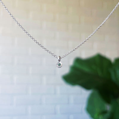 Green Sapphire Rise Necklace in Sterling Silver hanging in front of a white brick wall