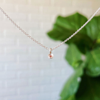 Orange Sapphire Rise Necklace in Sterling Silver hanging in front of a white brick wall