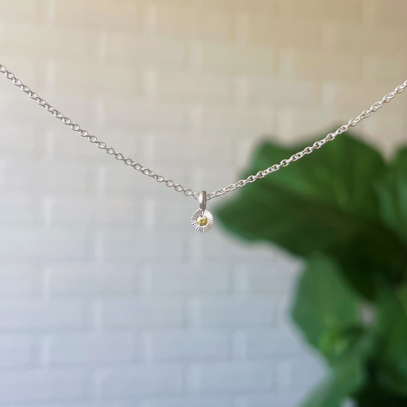 Yellow Sapphire Rise Necklace in Sterling Silver hanging in front of a white brick wall