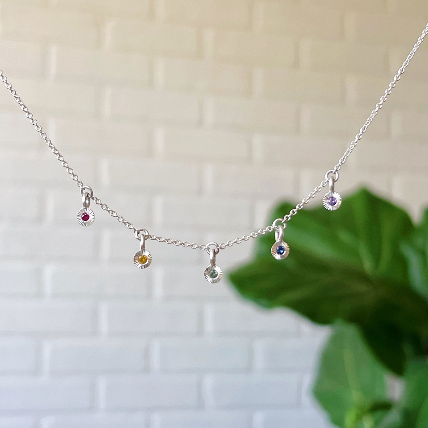 Rainbow Borealis Necklace in Sterling Silver hanging in front of a white brick wall