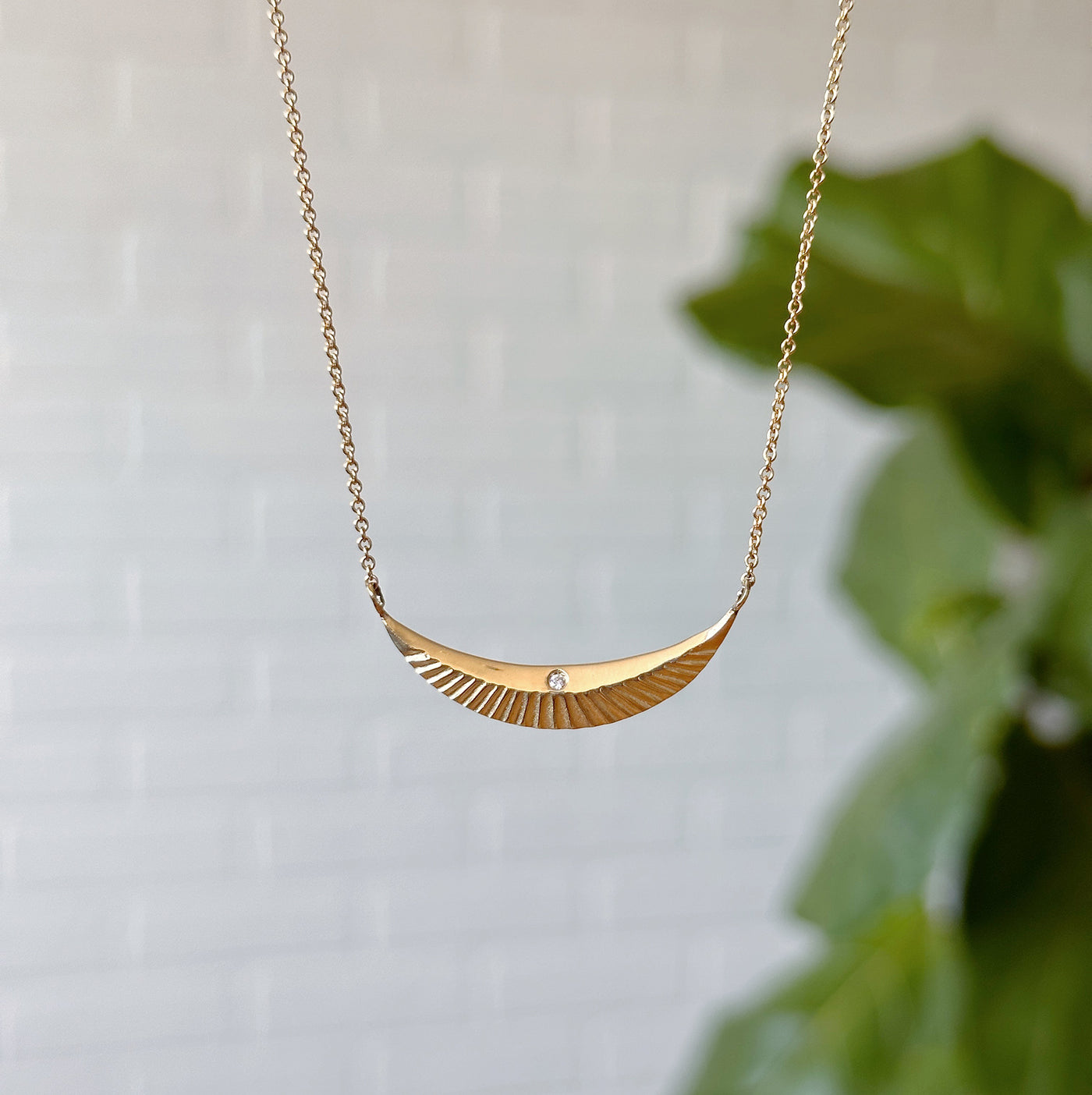 Gold and Diamond Icarus Necklace hanging in front of a white wall, front angle