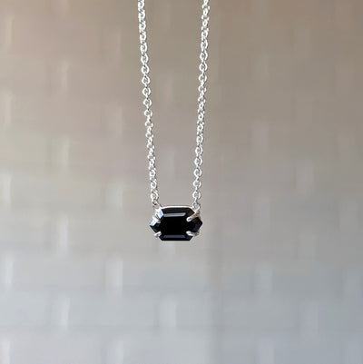 Emerson Black Garnet Necklace in Silver hanging in front of a white brick wall, front angle
