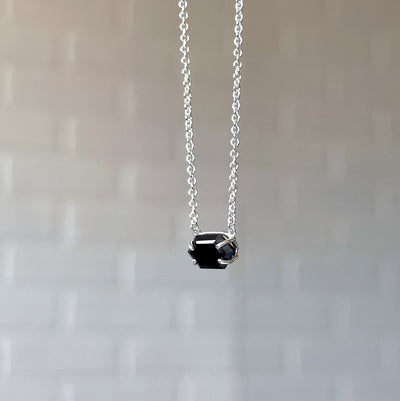Emerson Black Garnet Necklace in Silver hanging in front of a white brick wall, side angle