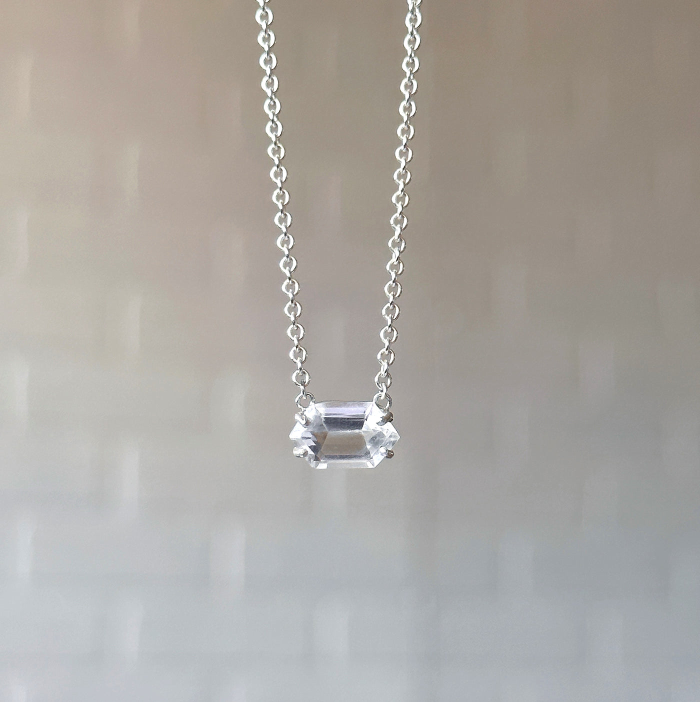 Emerson Quartz Necklace in Silver hanging in front of a white brick wall, front angle